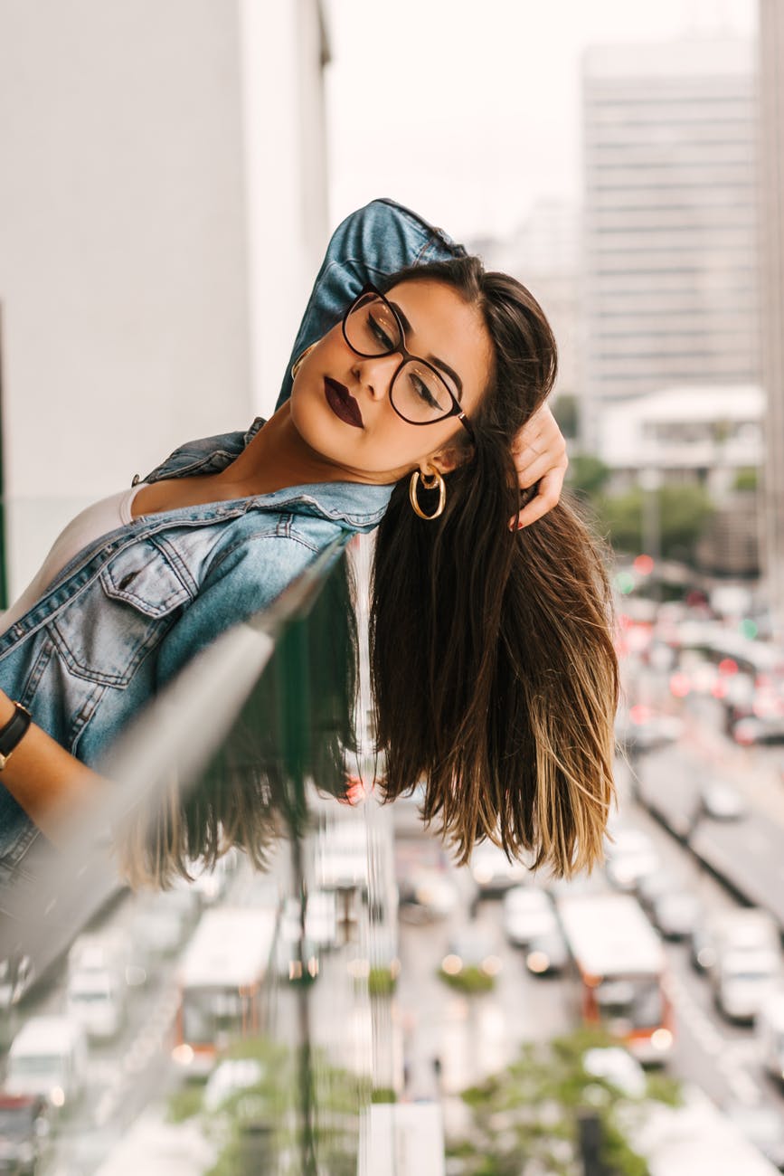 photo of woman leaning backwards on glass railing while holding her hair and looking down