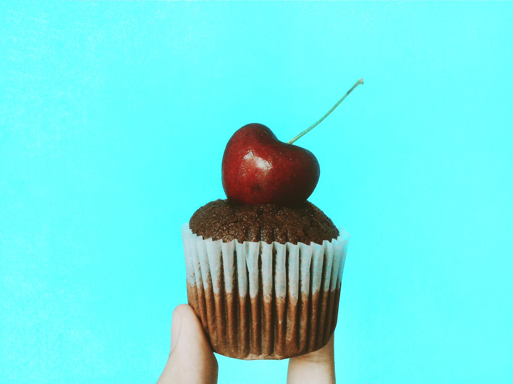 person holding chocolate cupcake with cherry topping
