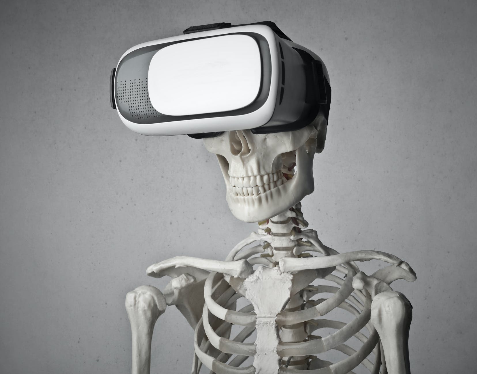 portrait photo of skeleton in front of gray background with white and black vr goggles on